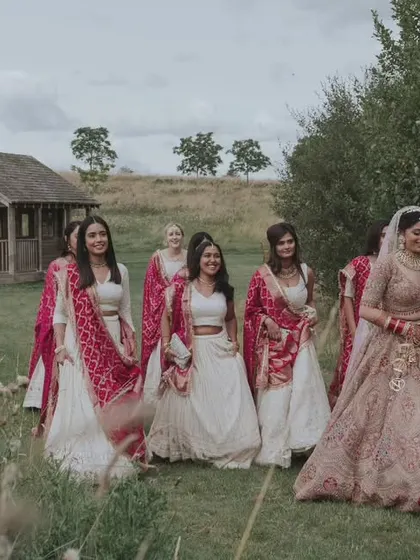 The bride and her bridesmaids sharing a laugh as they walk through the fields. This candid shot captures the fun and relaxed atmosphere of the day.