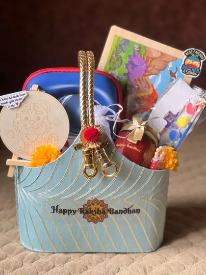 A straight-on shot of the blue Rakhi hamper, showcasing the beautiful "Happy Raksha Bandhan" text on the basket itself.