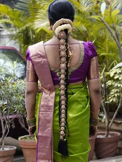 A beautiful view of a traditional bridal hairstyle from the back. The long braid is decorated with delicate gold and pearl accessories and topped with a classic jasmine veni.