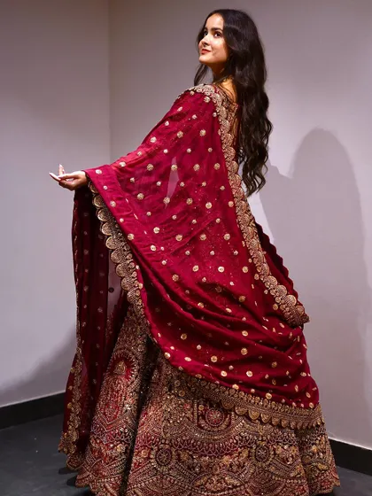 The back view of this bridal maroon lehenga shows off the stunning, heavily embroidered dupatta. The intricate gold work and sequin details are designed to look incredible from every angle.
