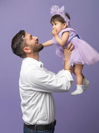 A father lifts his little girl into the air. Her little snack and happy expression make this a fun and authentic father-daughter moment.
