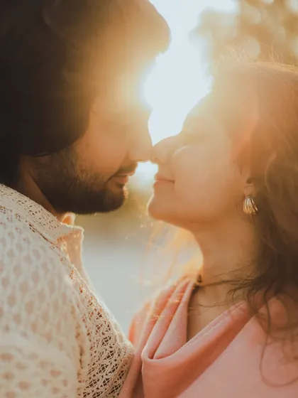 A classic romantic close-up with the sun creating a beautiful flare, highlighting the couple's intimacy as they touch noses.