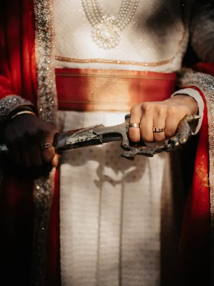 A close-up, dramatic shot of the groom's hands holding the traditional Maratha sword.