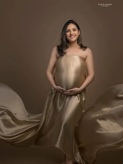 A stunning maternity portrait featuring a flowing golden satin drape. The makeup is kept soft and subtle to focus on the natural beauty and glow of motherhood.