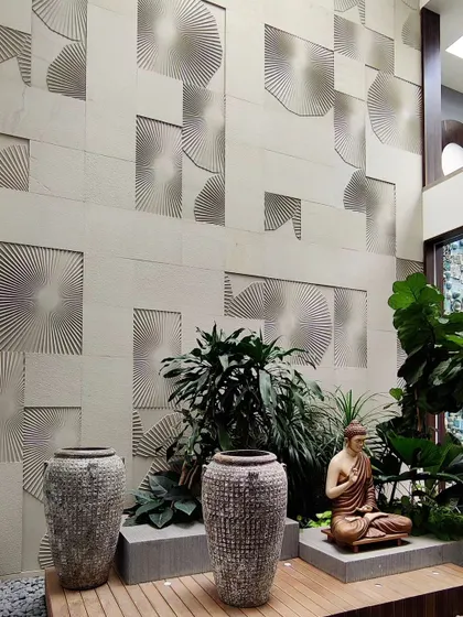This serene corner features a sandstone wall with an engraved fan pattern, creating a subtle yet beautiful texture. The Buddha statue and lush plants complete this tranquil meditation spot within the home's courtyard.