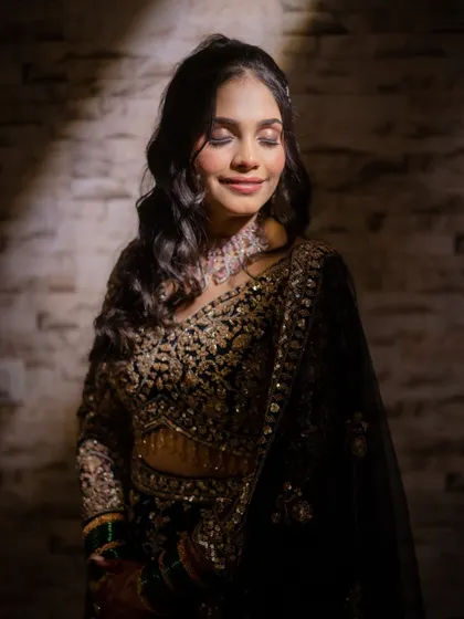 An artistic shot of the bride's sangeet look. The dramatic lighting highlights the intricate embroidery of her lehenga and the soft, shimmering makeup on her eyes.