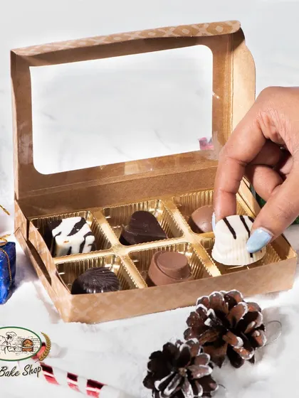 A hand selecting a white chocolate piece from our assorted soft-centered chocolate box. This shows the tempting variety available for your Christmas gifting needs.