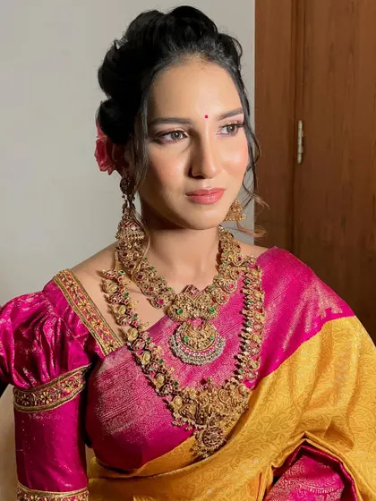 A picture-perfect moment capturing the essence of this soft glam look. The pink tones in the makeup harmonize beautifully with her yellow and pink saree and traditional temple jewellery.