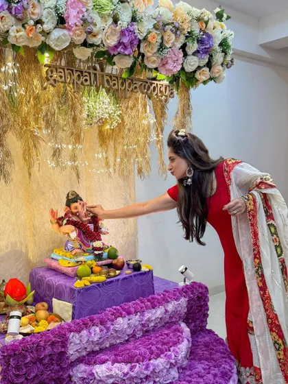 A candid moment of prayer in front of the purple and pastel floral Ganpati decor. This design creates a warm and inviting space for devotion and celebration.