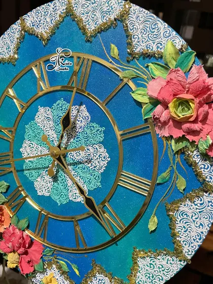 This clock features an ocean-themed blue gradient base with contrasting pink and yellow flowers. The white filigree pattern in the center and along the border adds a delicate, lace-like touch.