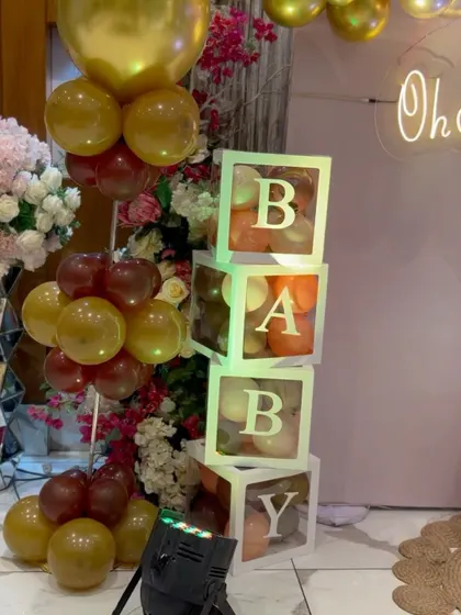 Light-up "BABY" blocks filled with balloons, next to an "Oh Baby" neon sign and a floral arrangement.