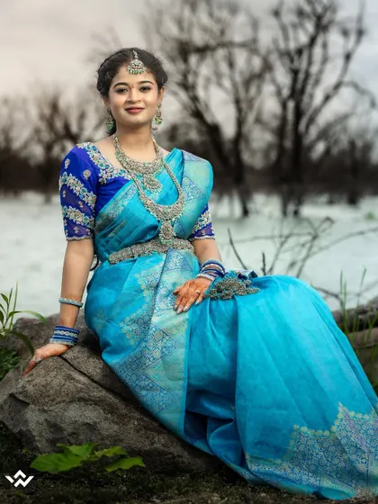 A stunning bridal portrait by the water. The vibrant blue of her saree contrasts beautifully with the moody sky, creating a dramatic and artistic image.