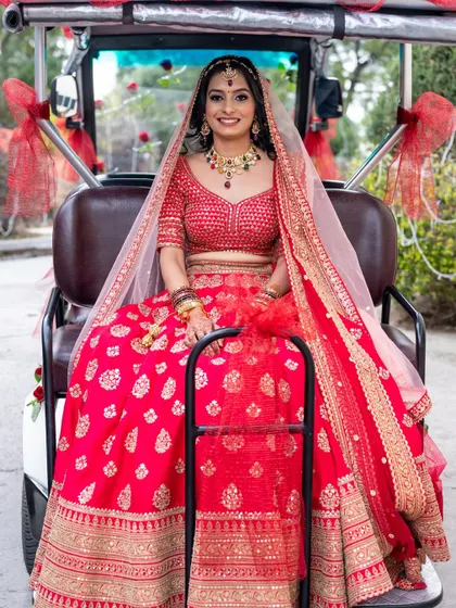 A stunning portrait of the bride in her classic red lehenga, seated in a decorated buggy.