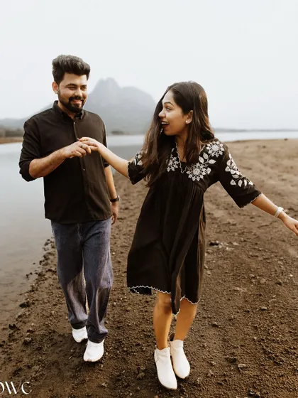 A candid moment of a couple walking and talking by the water, capturing their natural interaction.