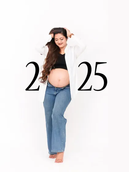 A modern and casual maternity portrait against a clean white background. The mom-to-be is styled in jeans and a crop top, creating a fresh and contemporary look for a 2025 due date announcement.