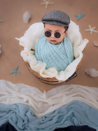 Cool, calm, and collected. This newborn is ready for the beach in his little cap and sunglasses, swaddled cozily in a basket.