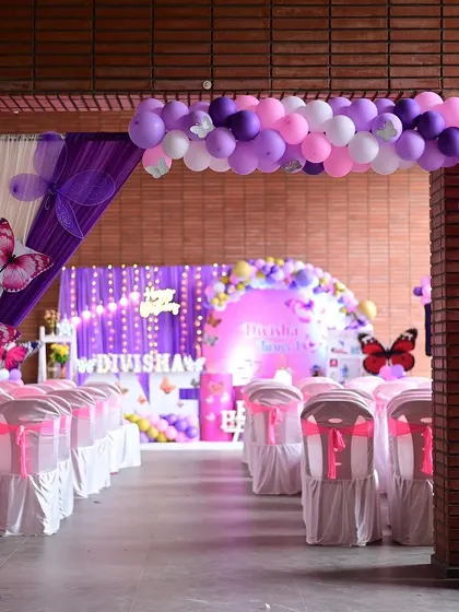 The entrance to this butterfly-themed party features a full balloon arch in shades of purple and pink, with matching drapery and butterfly cutouts to welcome guests.