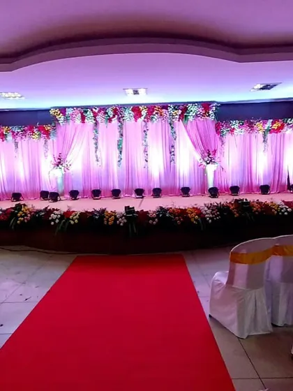 A classic reception stage setup featuring a long red carpet aisle. The backdrop of soft pink drapery, accented with a floral border and strategic uplighting, creates a timeless and elegant look.