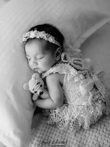 A timeless black and white portrait of a newborn in a delicate lace outfit, cuddling a tiny teddy bear. Monochrome photos emphasize emotion and texture beautifully.