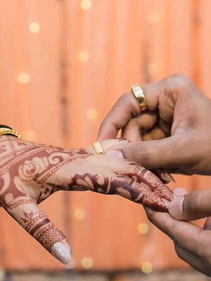 A macro shot of the ring exchange, focusing on the hands, the ring, and the bride's intricate henna. This highlights a key moment of the engagement ceremony.