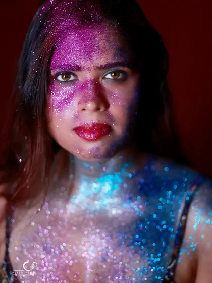 A powerful and direct portrait, adorned in a galaxy of blue and purple glitter. Her gaze is steady and confident, owning the artistic and bold look.