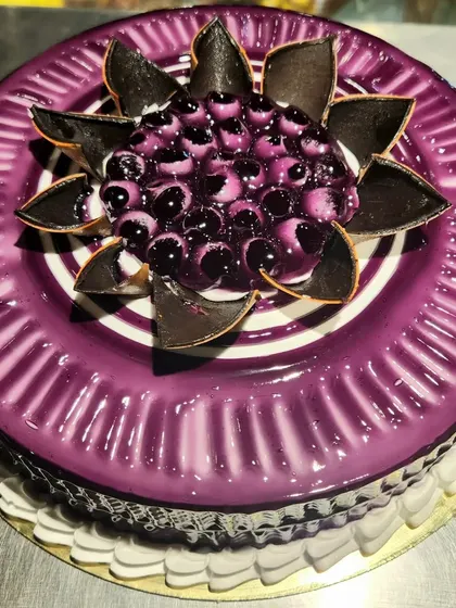 A glossy blueberry glaze cake. The top is decorated with a beautiful pattern of fresh blueberries and chocolate shards.