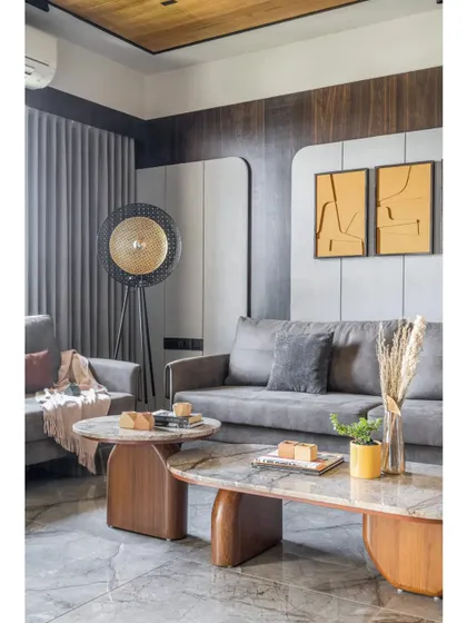 Another view of the living room, focusing on the interplay of materials. The marble coffee tables with their unique wooden bases stand out against the grey marble floor, adding a touch of organic form and natural luxury to the space.