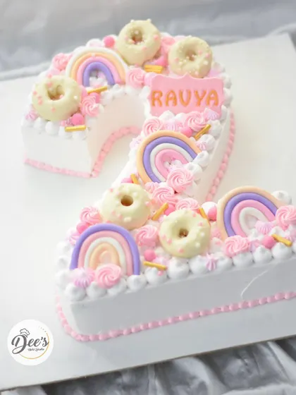A sweet and pretty number cake for a second birthday. This cake is shaped like the number two and decorated with mini donuts, rainbows, and pastel buttercream swirls.