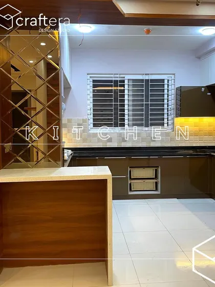 A view into a kitchen with a breakfast counter. The design features brown high-gloss cabinets, a tiled backsplash, and a mirrored panel on the side, creating a warm and inviting cooking space.
