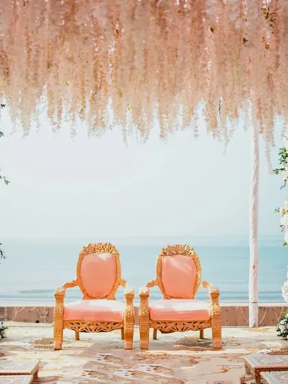A serene shot of the beachside wedding mandap before the ceremony begins. The elegant chairs, floral arrangements, and the ocean backdrop create a sense of peaceful anticipation.