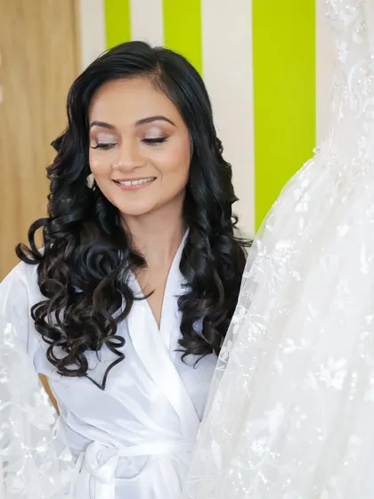 A moment of admiration as the bride looks at her wedding gown. Her makeup is soft and shimmery, with beautiful curls ready to be styled.