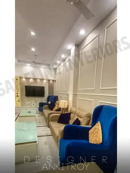 The seating area combines a beige sofa with bold blue accent chairs. The wall features French molding for a classic touch.