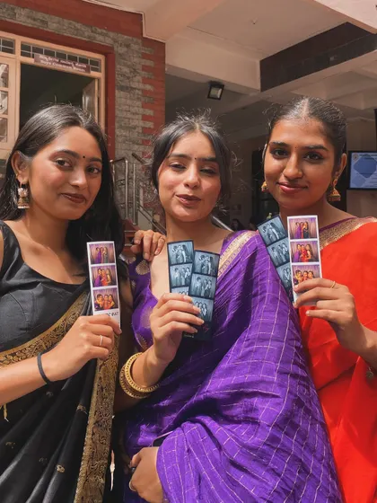 Students in beautiful sarees holding up their photo strips, a perfect memento from their Ethnic Day celebration.