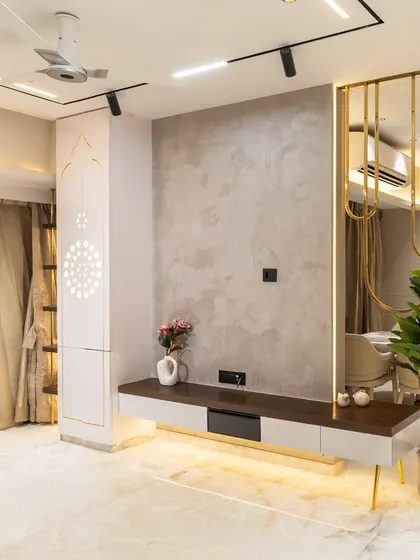 This open-concept living area balances form and function. A calming palette of muted neutrals meets gleaming gold accents and warm lighting. The graceful brass partition and sculptural lighting bring depth and drama, while indoor greens add a touch of serenity.