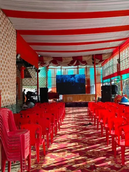 A pandal setup with red and white striped ceiling drapes and red plastic chairs. This is a practical and cost-effective setup for community gatherings.