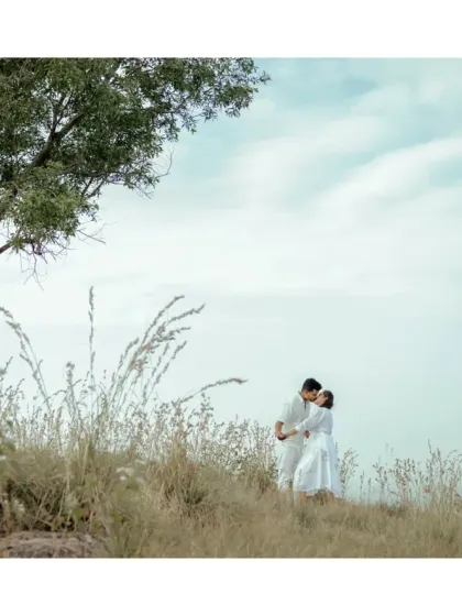 A dreamy, romantic shot of a couple embracing in a field of tall, dry grass. The soft, hazy light gives it a timeless and ethereal quality.