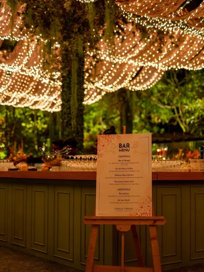 A beautifully lit bar setup for a Christmas event. The bar menu is displayed on an easel, and the ceiling is adorned with a canopy of fairy lights.