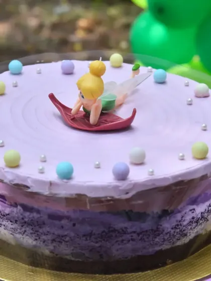 A close-up of a fairy-themed birthday cake. The delicate Tinkerbell topper and pastel-colored pearls make this a magical centerpiece for the dessert table.