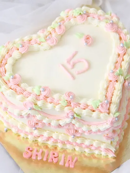 A lovely heart-shaped cake for a 15th birthday. This design features delicate pink, cream, and light green piping, creating a soft and romantic vintage look.