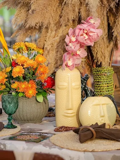 A close-up of a tablescape, featuring unique Tiki-faced vases, pink orchids, and pampas grass. These details show a deep commitment to the theme.
