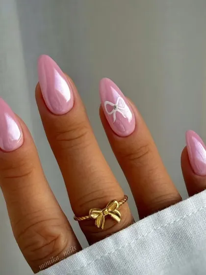 Nail inspiration for coquette nails, featuring a pearlescent pink base and a simple white bow accent.