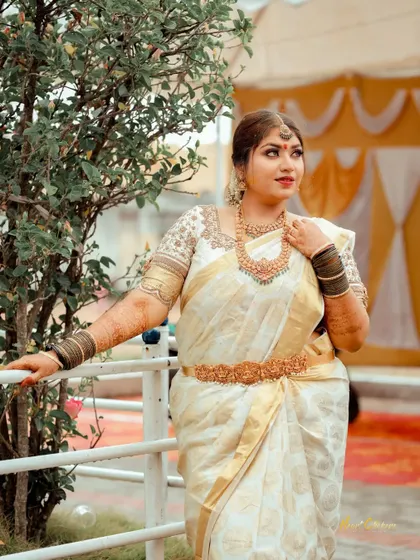 A candid outdoor portrait of the bride in a stunning white and gold saree. The natural light and setting add a fresh, airy feel.