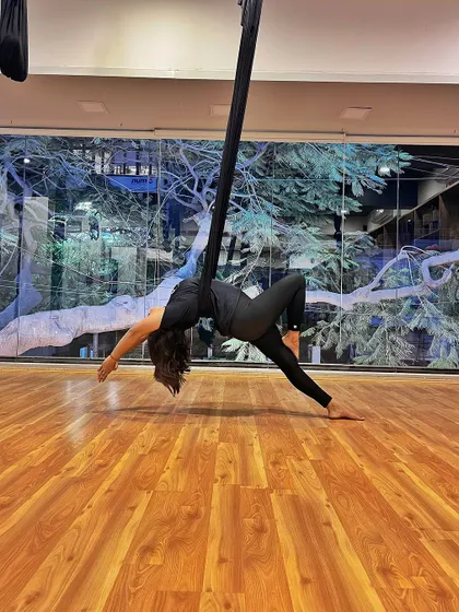 A beautiful shot of a student in a side-bending aerial pose, with the natural light from the window creating a serene backdrop.
