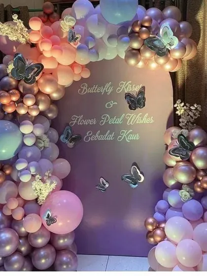 A close-up of the elegant butterfly-themed setup with a pastel purple backdrop and a balloon arch in shades of pink and purple.