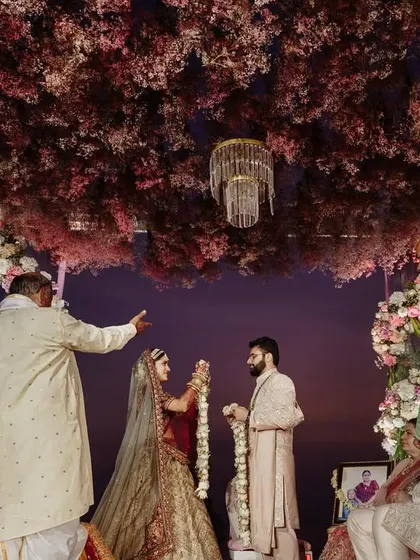 The couple shares a look during their Varmala ceremony. The twilight sky and the stunning floral decor provide a romantic and dramatic backdrop for this pivotal moment.