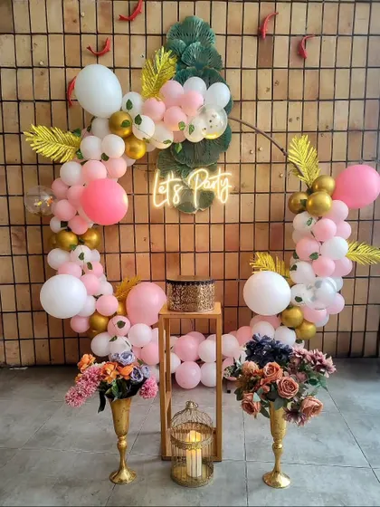 A "Let's Party" neon sign set against a circular frame with pink and gold balloons. Neon signs are a great way to add a modern, fun touch.
