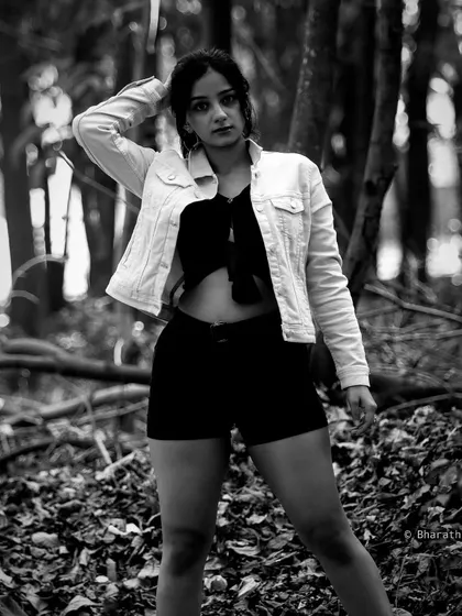 A full-body shot of a model in a denim jacket and shorts, set in a wooded area. The black and white conversion enhances the textures of the foliage and the outfit.