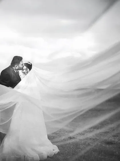 A classic black and white portrait using the bride's long veil to create a sense of movement and intimacy. The sweeping fabric against the open landscape adds a layer of drama and romance to this tender moment.