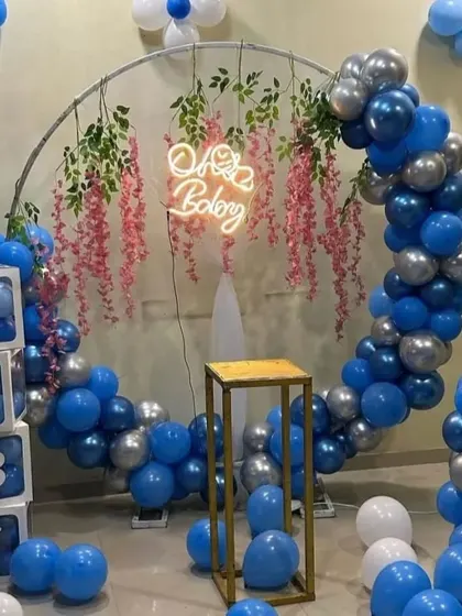 A stylish 'Oh Baby' shower for a baby boy. A circular frame is decorated with blue and silver balloons and hanging floral elements, complemented by 'BABY' blocks.