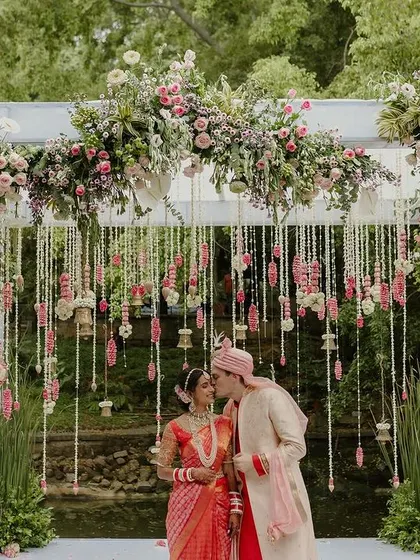 A beautiful moment captured at the mandap, where the couple is framed by hanging floral strings and lush arrangements, blending tradition with romance.